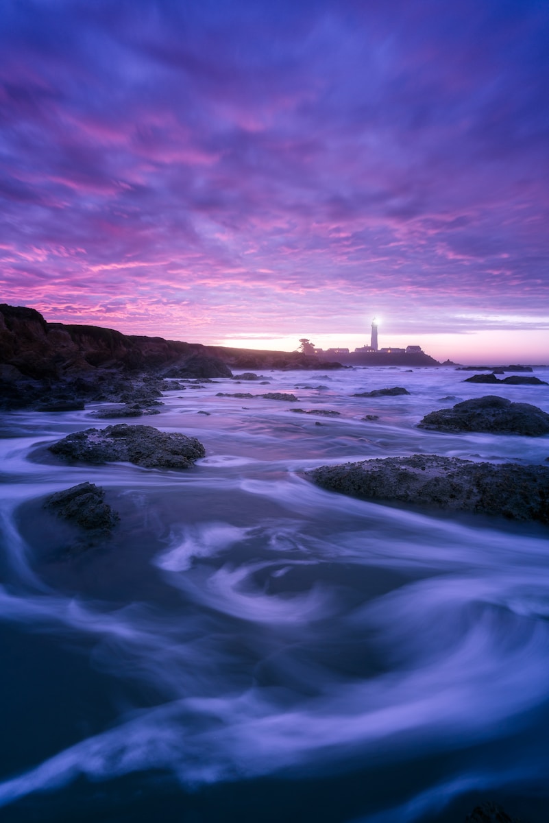 rocks and sea with silhouette of lighthouse in background